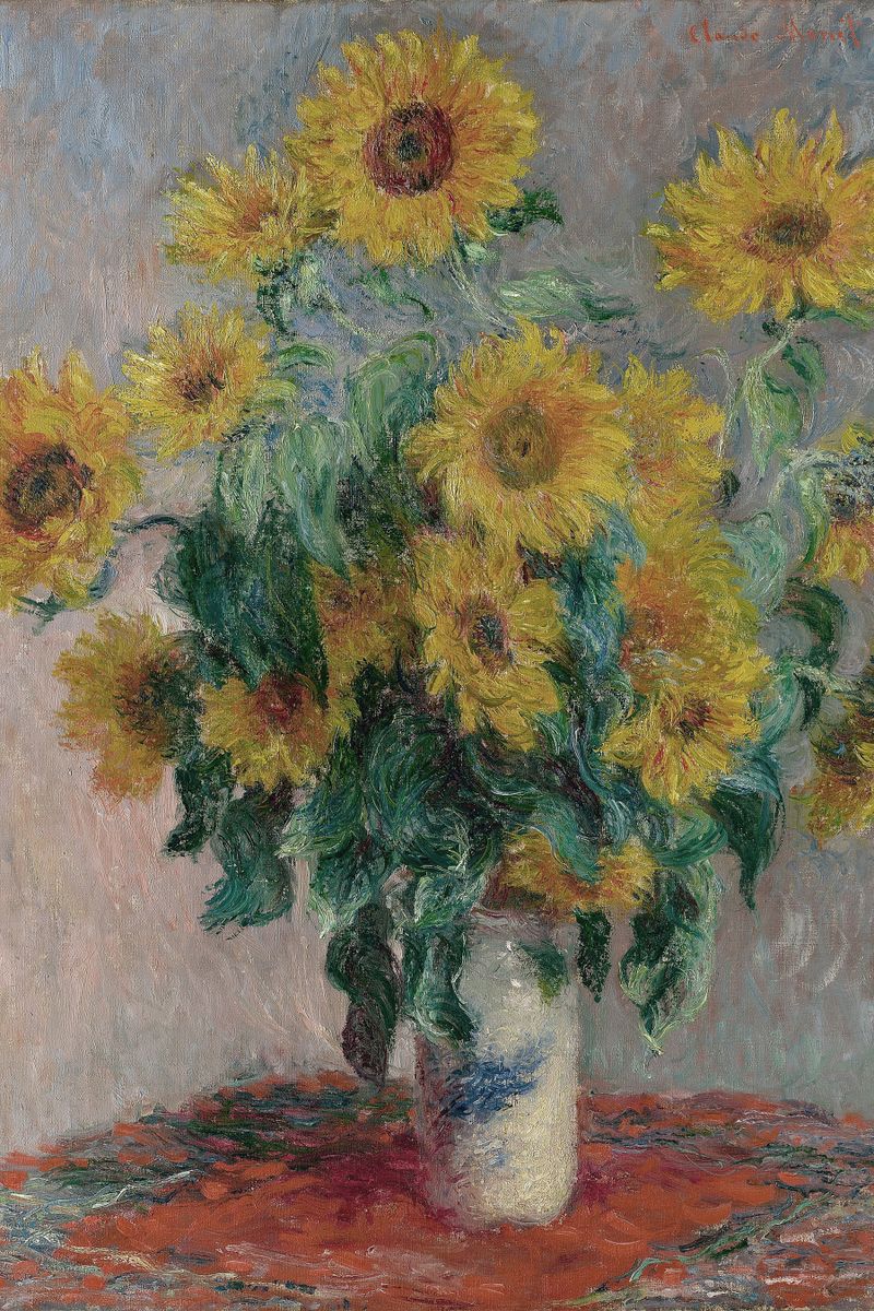 A bouquet of sunflowers in a white ceramic vase on a red-draped table against a gray-blue wall.