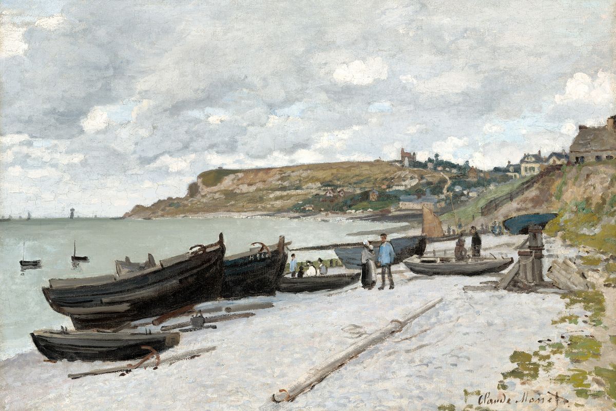 Several dark wooden fishing boats resting on a pale pebble beach with figures nearby and a chalk headland village in the back