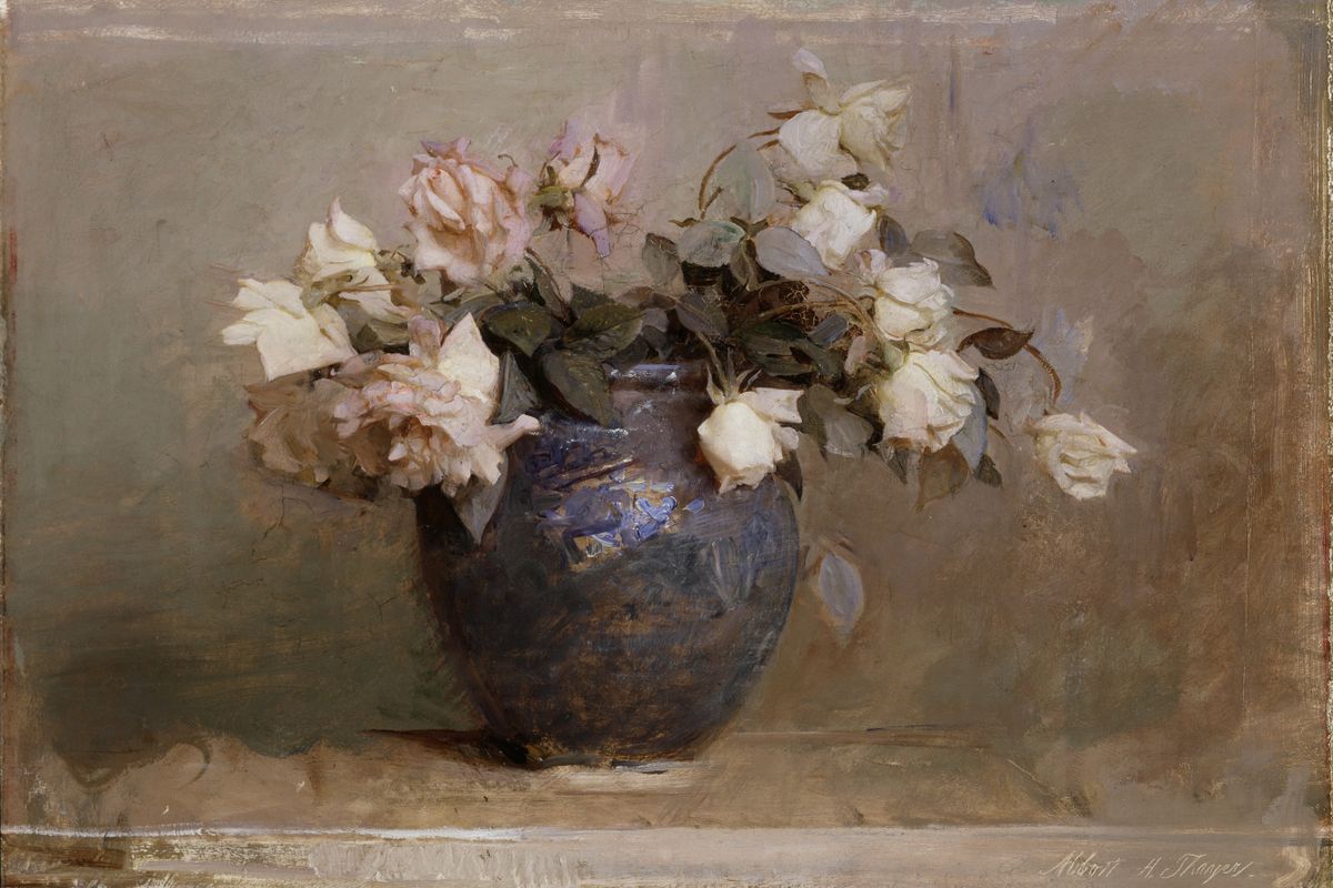 A dark glazed ceramic jar holding an overflowing arrangement of blush and ivory roses on a stone ledge.