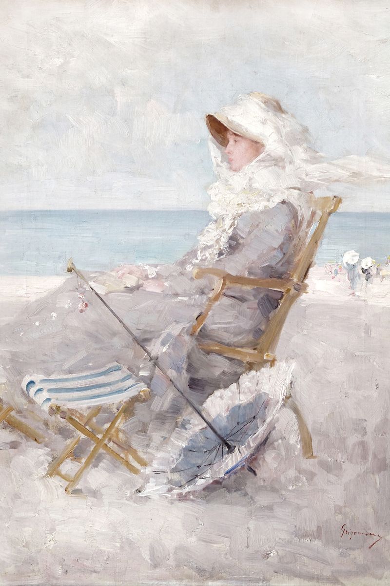 A woman in Victorian dress and a veiled white hat sits in a folding beach chair on sandy shore, holding a parasol, with calm