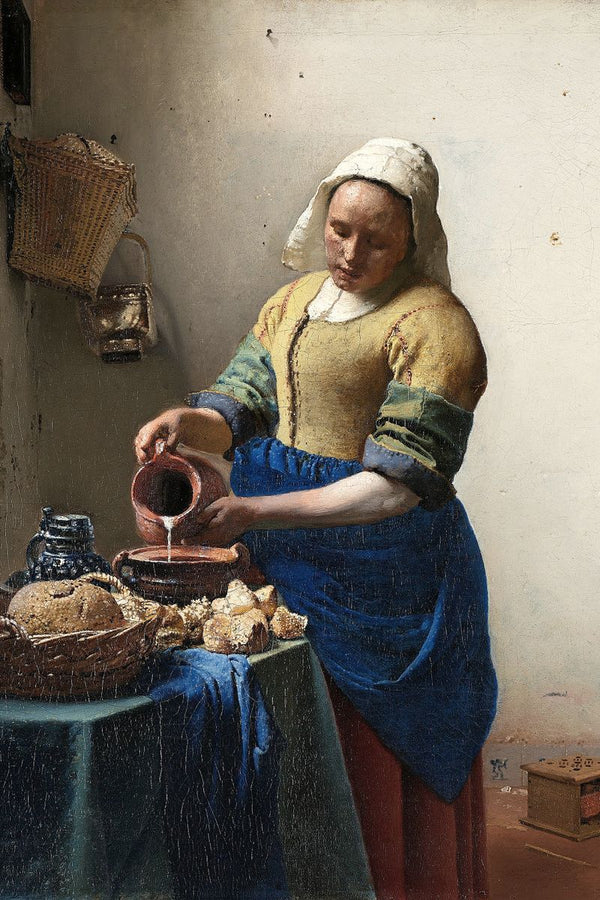A woman in a white cap pours milk from a clay jug into a bowl on a table with bread in a sparse kitchen.